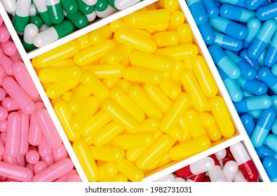 Top View Of Yellow, Blue, Pink, Red, Green, And White Capsule Pills In Plastic Box Texture Background. Pharmacy Shop Product. Vitamins And Supplements. Antibiotic Drug Selection. Capsule Pill Industry