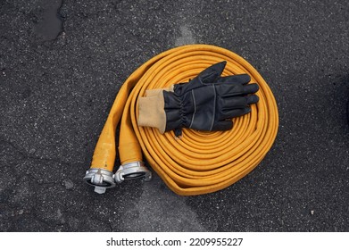 Top View Of Yellow Fire Hose With Black Gloves On It On The Ground.