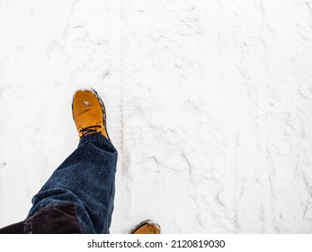 top view of yellow leather boot on snow-covered path on overcast winter day