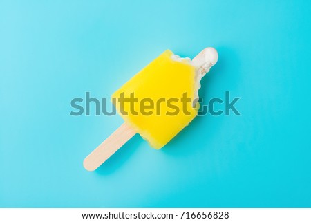 top view yellow popsicle with bites on a blue background