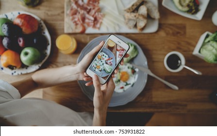 Top view of youn hipster girl taking photo of food via her smartphone, blogger woman taking photo of breakfast on her mobile - Powered by Shutterstock