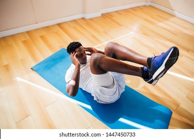 Top View Of Young African American Man Doing Sit-up Exercise On Yoga Mat At Gym. Male Fitness Model Performing Crunch At Fitness Center