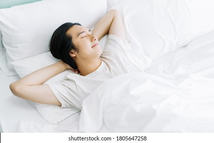 Top view of young Asian man smiling while sleeping in his bed and relaxing in the morning. Rest relax good mood lifestyle concept.