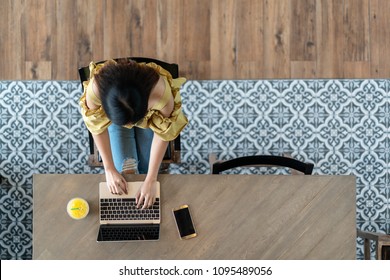 Top View Of Young Asian Woman Sitting, Using Laptop In Modern Workplace, Café Coffee Shop. Urban Female College Lifestyle Concept On Wooden Table, Blue Vintage Floor Tile Pattern With Copy Space.