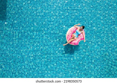Top view of young asian woman in swimsuit on the pink donut lilo in the swimming pool.