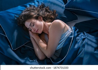 Top view of young beautiful woman dreaming in bed and relaxing at night. High angle view of woman with closed eyes sleeping well at home in the dark. Beautiful girl sleeping peacefully under late.