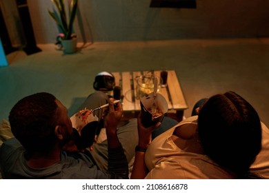 Top View Of Young Black Couple Eating Fast Food And Watching TV On Sofa At Home. Concept Of Domestic Entertainment And Leisure. Idea Of Relationship And Spending Time Together. Evening Or Night Time