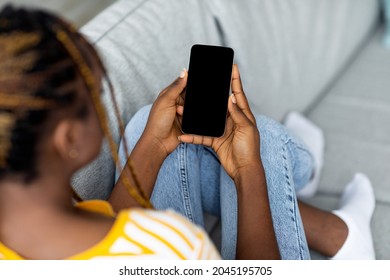 Top View Of Young Black Woman With Stylish Long Braids Using Brand New Cellphone With Empty Screen While Chilling On Couch At Home, Enjoying Newest Dating Mobile Application, Copy Space