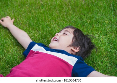 Top view of  young boy laying down on lawn in the park, Cropped shot Active child closing his eyes and laughing while lying on green grass field, Kid having fun playing outdoors in sunny day summer