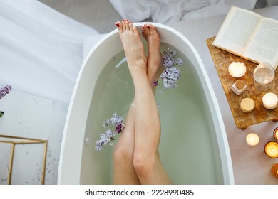 Top view of the young brunette woman reading the book and drinking white wine in bath with foam and candles - Powered by Shutterstock