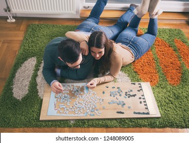 Top view of young couple laying on floor and doing puzzle