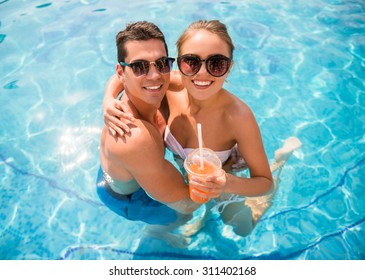 Top View Of Young Couple Relaxing In Resort Swimming Pool And Drinking Cocktails.