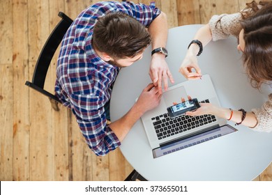 Top View Of Young Couple Sitting At Round Table And Using Laptop And Cell Phone