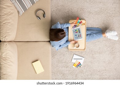 Top view of young creative female designer sitting on the floor by couch and choosing colors from palette for new logo on tablet display - Powered by Shutterstock