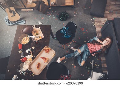 Top view of young drunk woman lying on floor in messy room