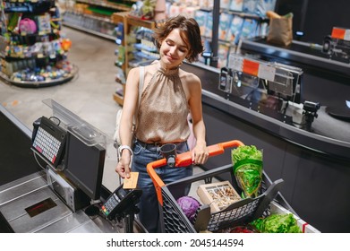 Top view young fun woman in casual clothes mask shopping at supermaket stand at store checkout giving credit card to cashier pay inside hypermarket. People lifestyle purchasing gastronomy food concept
