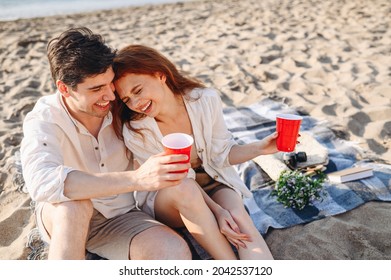 Top View Young Happy Couple Family Two Man Woman In White Clothes Hug Sitting On Sand Plaid Have Picnic Drink Hold Red Cups Rest Together At Sunrise Over Sea Beach Ocean Outdoor Seaside In Summer Day