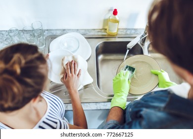 Top view of young happy couple is washing dishes while doing cleaning at home.