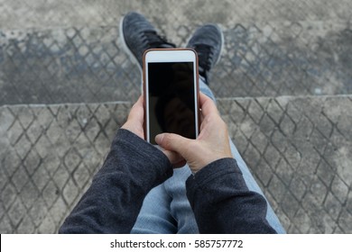 Top view of a young hipster business in jeans is using white mobile phone in hand  sitting at stairs. - Shutterstock ID 585757772