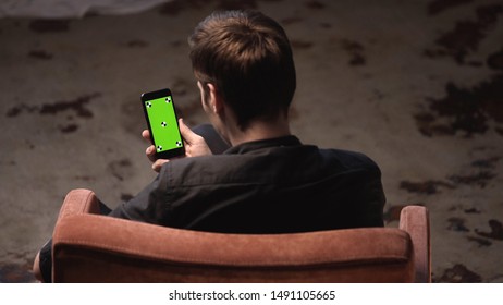 Top View Of Young Man With Brown Hair Sitting In Chair And Tapping On IPhone Green Screen In Dark Room. Stock Footage. Chroma Key