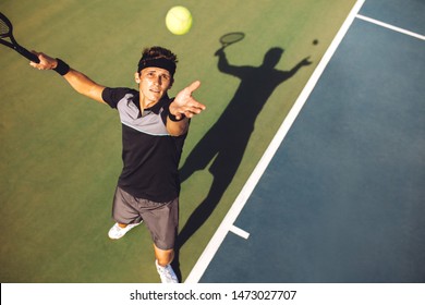 Top view of young man playing tennis tossing up the ball for the serve. Tennis player serving the ball in a match. - Powered by Shutterstock