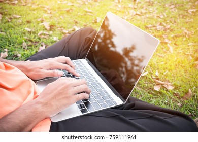 Top view of young man sitting in park on green grass with laptop computer, student studying searching information at outdoors. Copy space for text. E-Learning concept