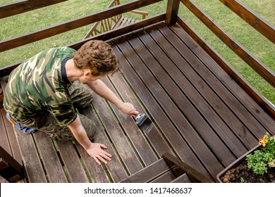 Top view of young man staining garden terrace wooden boards outdoors in spring. Terrace wood stain concept.
