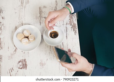 Top view of young  man using mobile phone sitting by cafe table drinking coffee and eating cookies