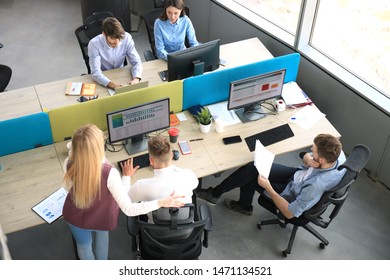 Top view of young modern colleagues in smart casual wear working together while spending time in the office.