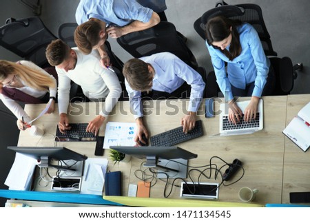 Top view of young modern colleagues in smart casual wear working together while spending time in the office.