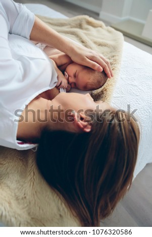 Mutter umarmt Neugeborenes auf dem Bett liegend