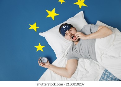 Top view young sad latecomer man 20s wear pajamas jam sleep mask rest at home lies wrap covered under blanket hold face slept late isolated on dark blue sky background Bad mood night bedtime concept