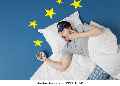 Top view young sad latecomer man wear pajamas jam sleep mask rest at home lies wrap covered under blanket spread hands slept late isolated on dark blue sky background Bad mood night bedtime concept
