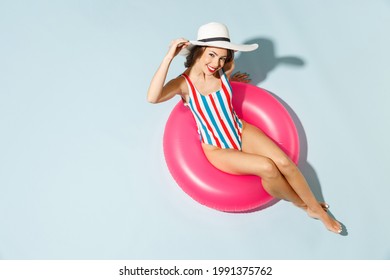 Top view young sexy woman slim body wear striped one-piece swimsuit wide brim hat lies inflatable tube ring hotel pool isolated on pastel blue color background Summer vacation sea rest sun tan concept