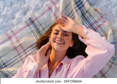 Top View Of A Young Smiling Beautiful Woman Relaxing On The Beach, Laying On Blanket