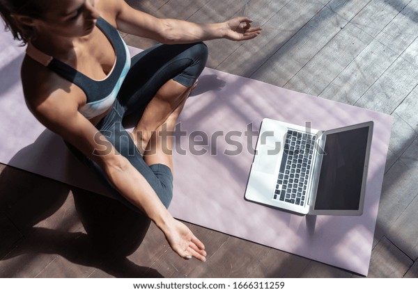 Top view young sporty slim woman coach internet\
video online training hatha yoga instructor modern laptop screen\
meditate Sukhasana posture relax breathe easy seat pose gym healthy\
lifestyle concept.