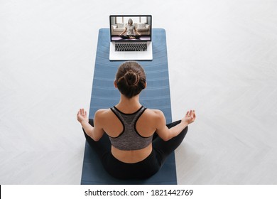 Top View Young Sporty Woman Using Laptop For Training Hatha Yoga With Virtual Instructor, Doing Sukhasana, Relax And Breathe Easy. Online Fitness, Workout At Home. Wellness, Active Lifestyle Concept