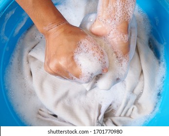 Top View Of Young Woman To Fabric Washing With Hand To Clean Dirty Clothes Laundry With Bubbles Of Detergent And Water In Blue Basin.