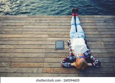 Top view young woman lying on a wooden jetty enjoying the sunshine,tourist girl in bright glasses lying on jetty by river, vintage photo of relaxing young woman in nature with tablet, cross process - Powered by Shutterstock