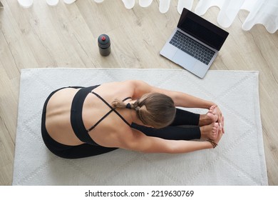 Top view of young woman practicing yoga, sitting in Seated forward bend exercise, paschimottanasana pose, working out, wearing sportswear - Powered by Shutterstock