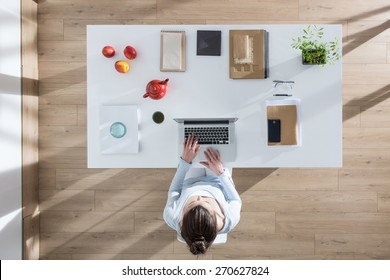 top view, young woman sitting at desk and working on her laptop, her table is perfectly tidy, the sun casts graphics shadows on the wood floor