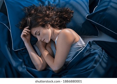Top view of young woman sleeping on side in her bed at night. Beautiful girl sleeping profoundly and dreaming at home with blue blanket. High angle view of woman asleep with closed eyes. - Shutterstock ID 1886880001