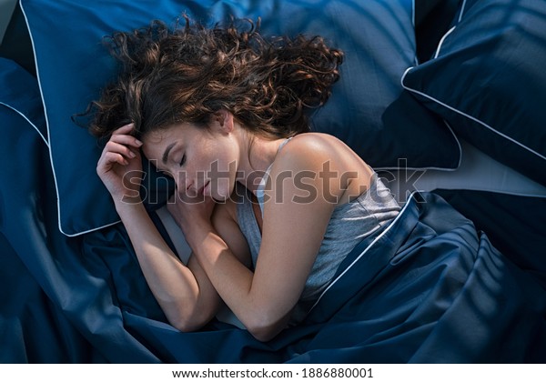 Top\
view of young woman sleeping on side in her bed at night. Beautiful\
girl sleeping profoundly and dreaming at home with blue blanket.\
High angle view of woman asleep with closed\
eyes.