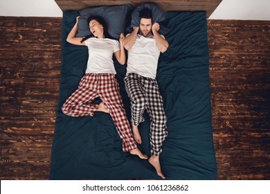 Top View. Young Woman Snores Loudly And Prevents Irritated Man From Sleeping. Family Snoring Concept. Problem Of Loud Snoring. Couple's Sleep Concept. Rest At Home.