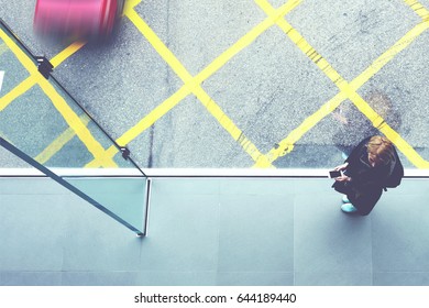 Top View Of A Young Woman Student With Mobile Phone In Hands Is Standing On Cross Street Walking Bridge With Asphalt Road And Hong Kong Taxi Car On Background. Copy Space For Your Advertising Content