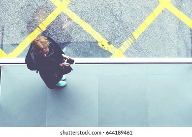 Top View Of A Young Woman Student With Mobile Phone In Hands Is Standing On Cross Street Walking Bridge With Asphalt Road And Hong Kong Taxi Car On Background. Copy Space For Your Advertising Content