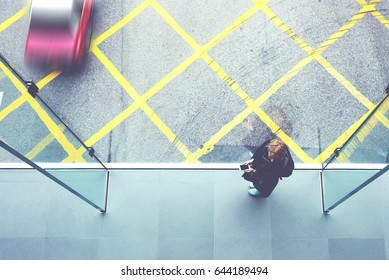 Top View Of A Young Woman Student With Mobile Phone In Hands Is Standing On Cross Street Walking Bridge With Asphalt Road And Hong Kong Taxi Car On Background. Copy Space For Your Advertising Content