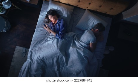 Top View: Young Woman Uses Smartphone in Bed at Night When Her Male Partner Trying to Fall Asleep Beside. Couple Fight, Argue. Addictive World of Social Media, Doom Scrolling, Fake News.
