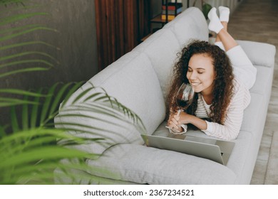 Top view young IT woman wear casual clothes lay down on grey sofa couch use laptop pc computer drink wine stay at home hotel flat rest relax spend free spare time in living room indoor. Lounge concept - Shutterstock ID 2367234521