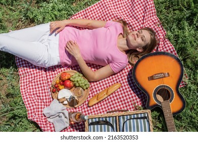 Top View Of Young Woman In White Pants Outside Having Picnic, Eating And Playing Guitar